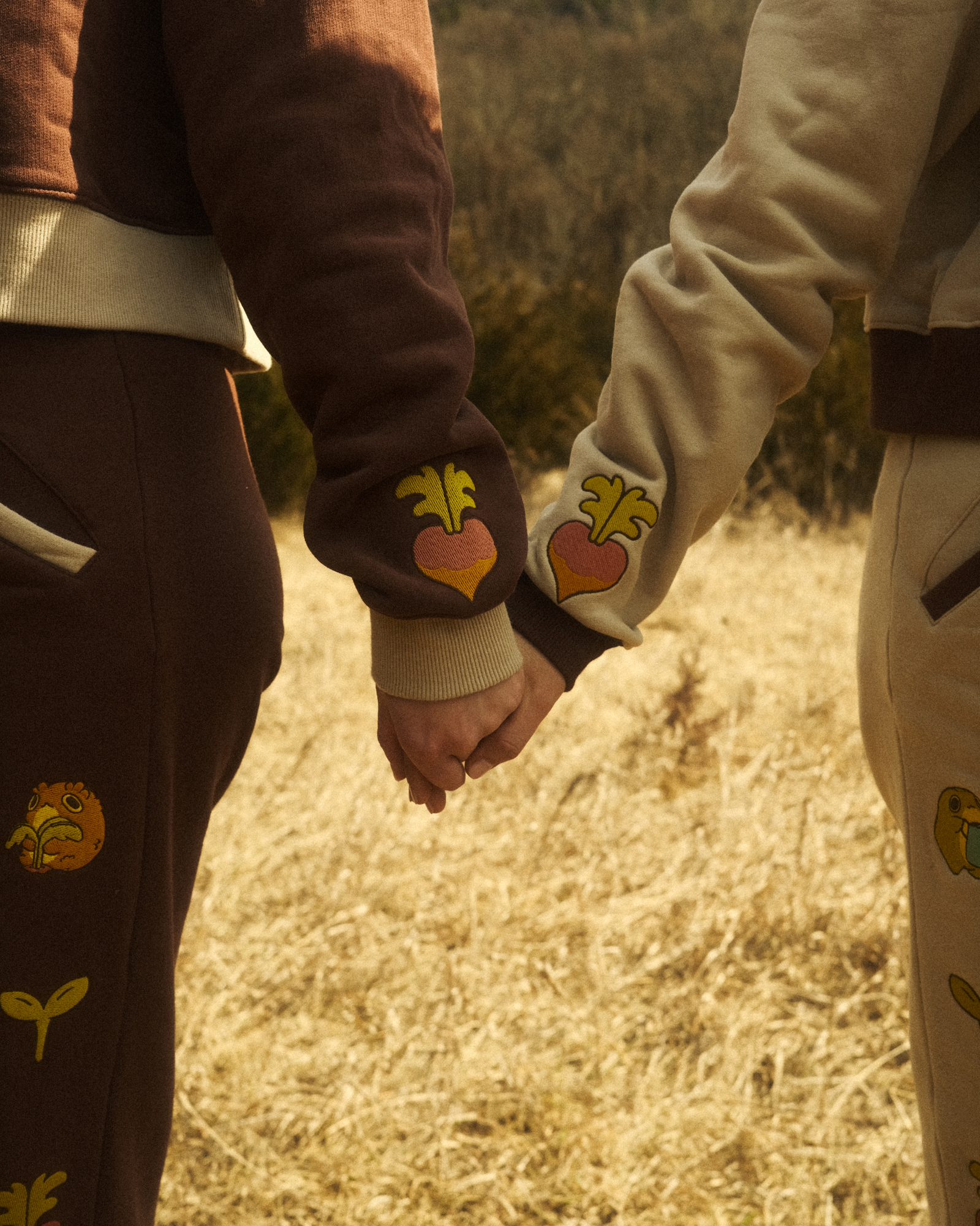 two people holding hands wearing sweaters with embroidered turnips on the sleeves