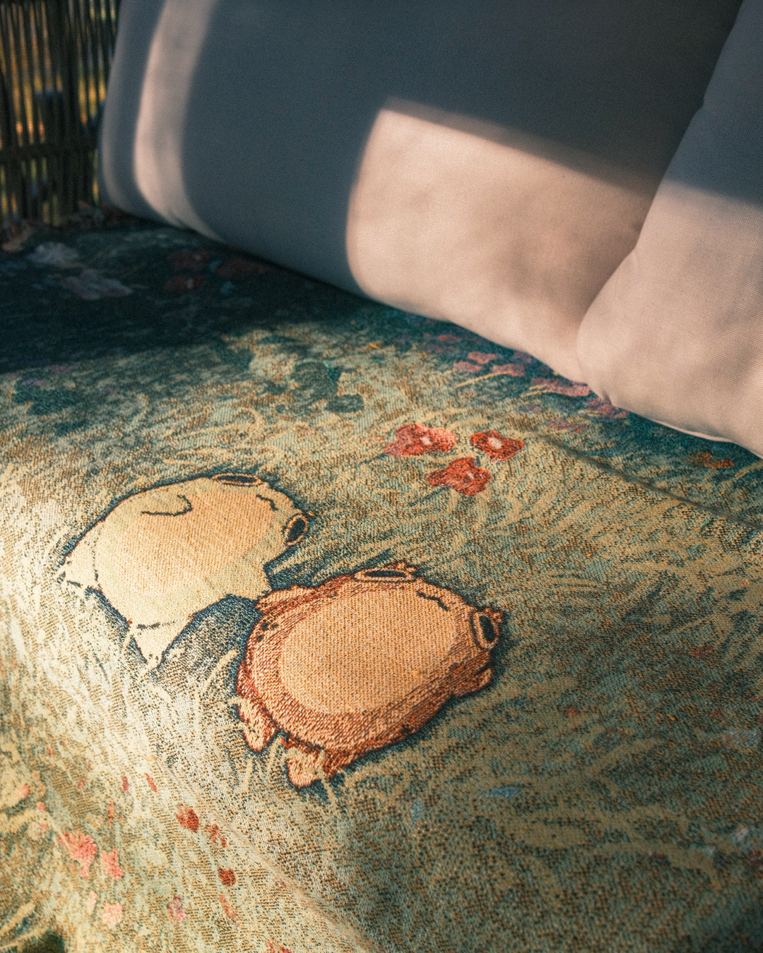 closeup of blanket of two frogs holding hands in a flowery field, blanket is on a couch