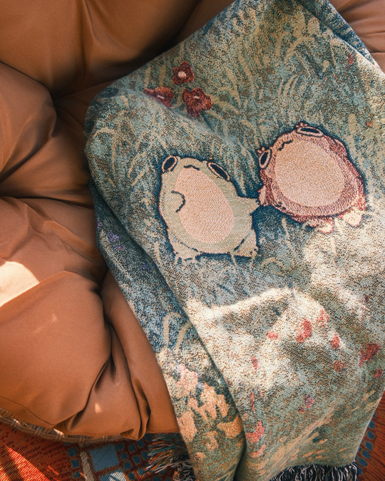 closeup of blanket of two frogs holding hands in a flowery field, blanket is on a chair