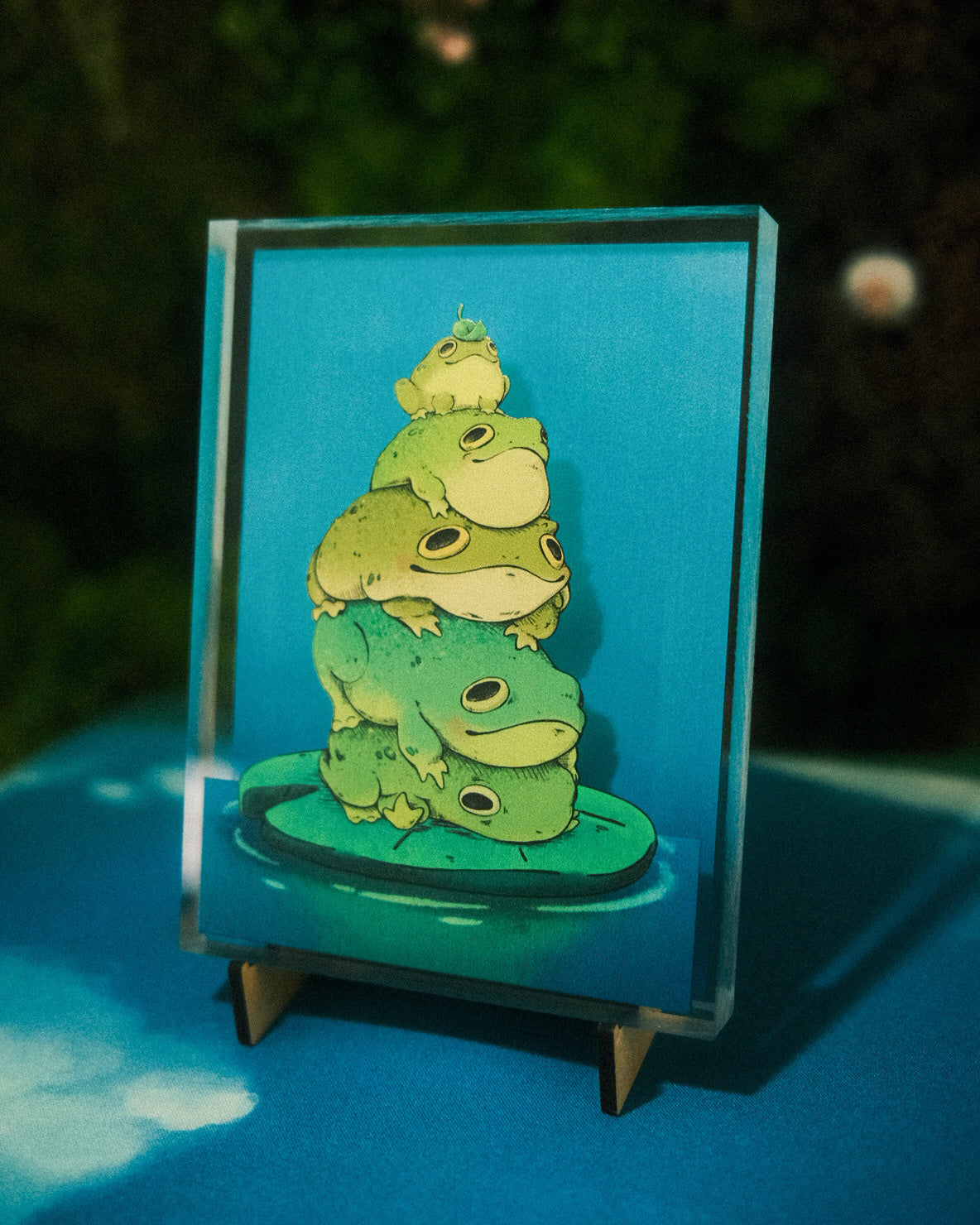 Stack of green frogs on a stand with a blue background