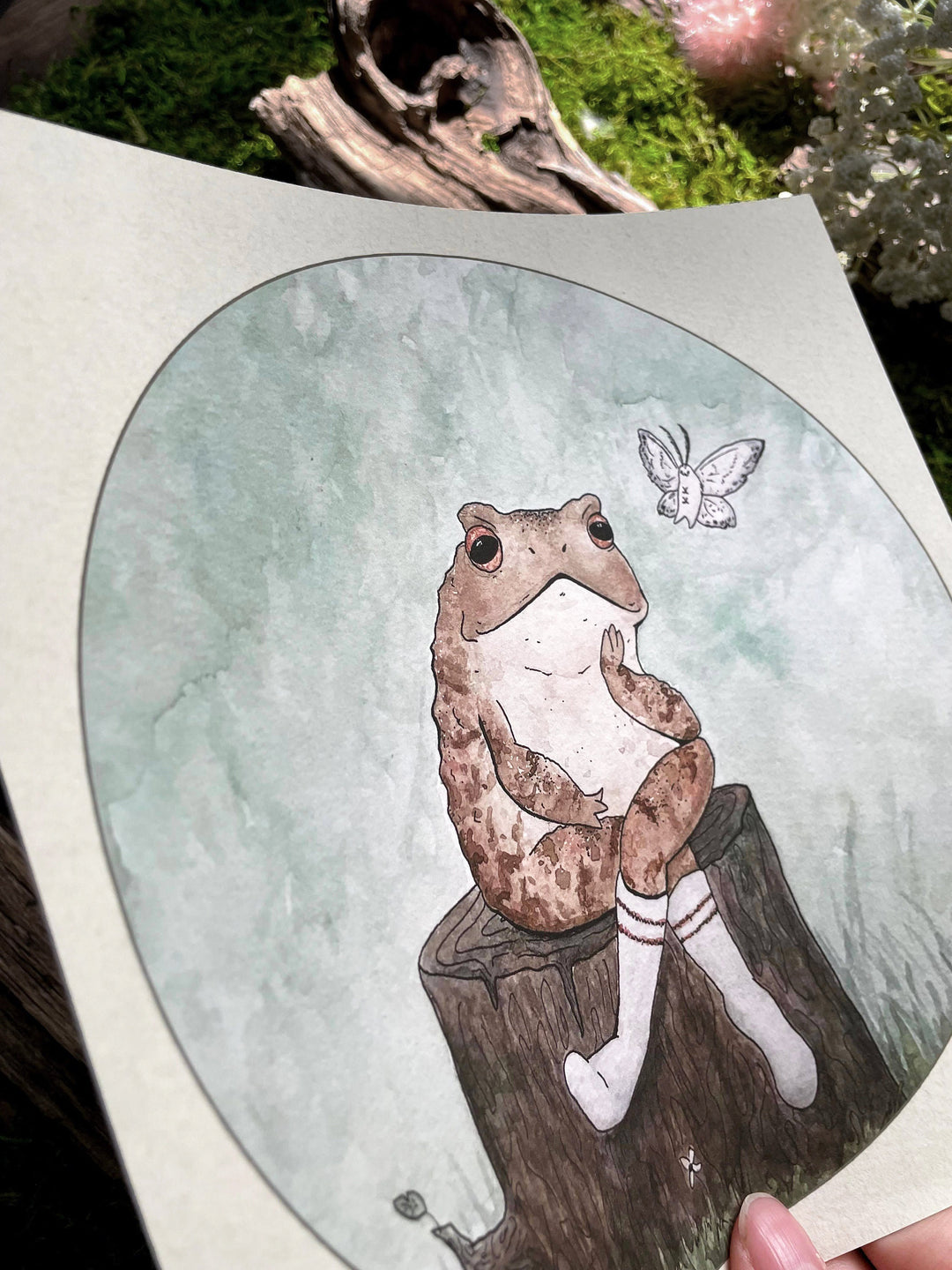 watercolor print with frog sitting on log next to a moth closeup