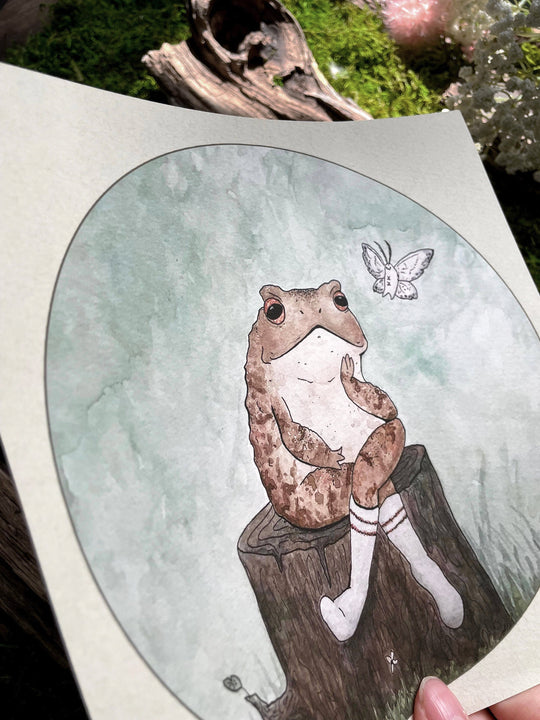 watercolor print with frog sitting on log next to a moth closeup