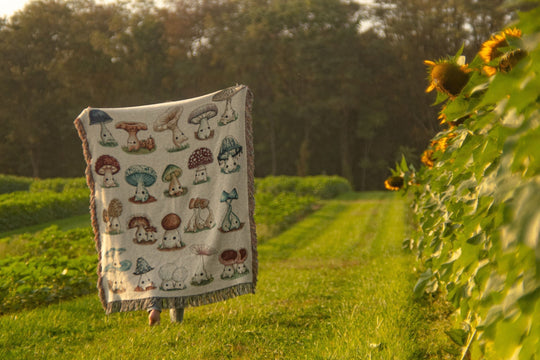 woven blanket with mushroom characters on it in a sunflower field