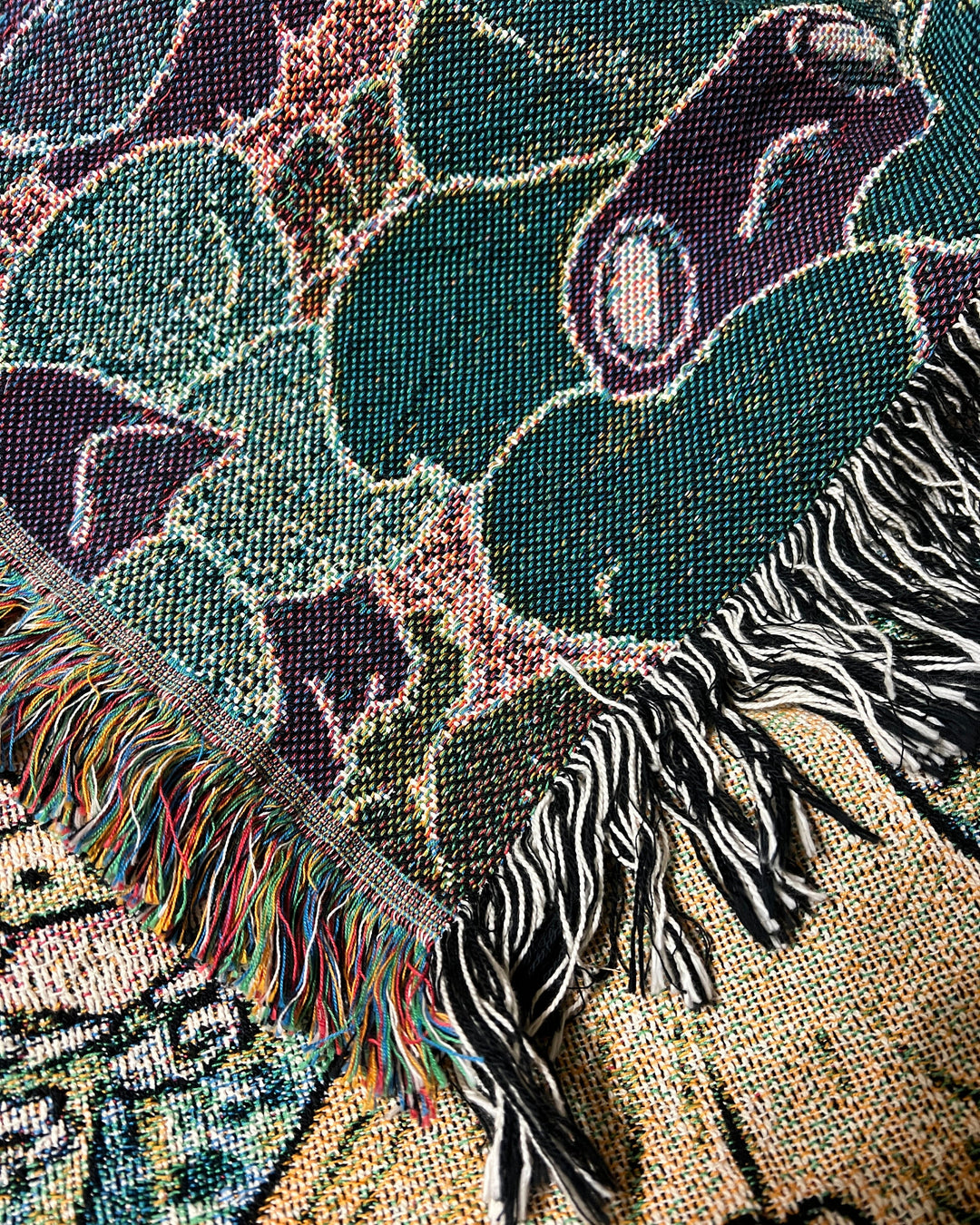 a woven blanket with a chanterelle character surrounded by frogs in flower necklaces closeup showing reverse side with inverted colors