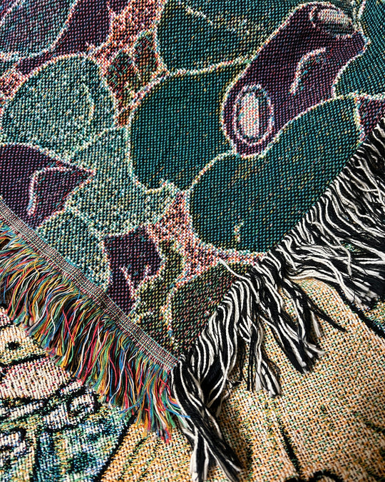 a woven blanket with a chanterelle character surrounded by frogs in flower necklaces closeup showing reverse side with inverted colors