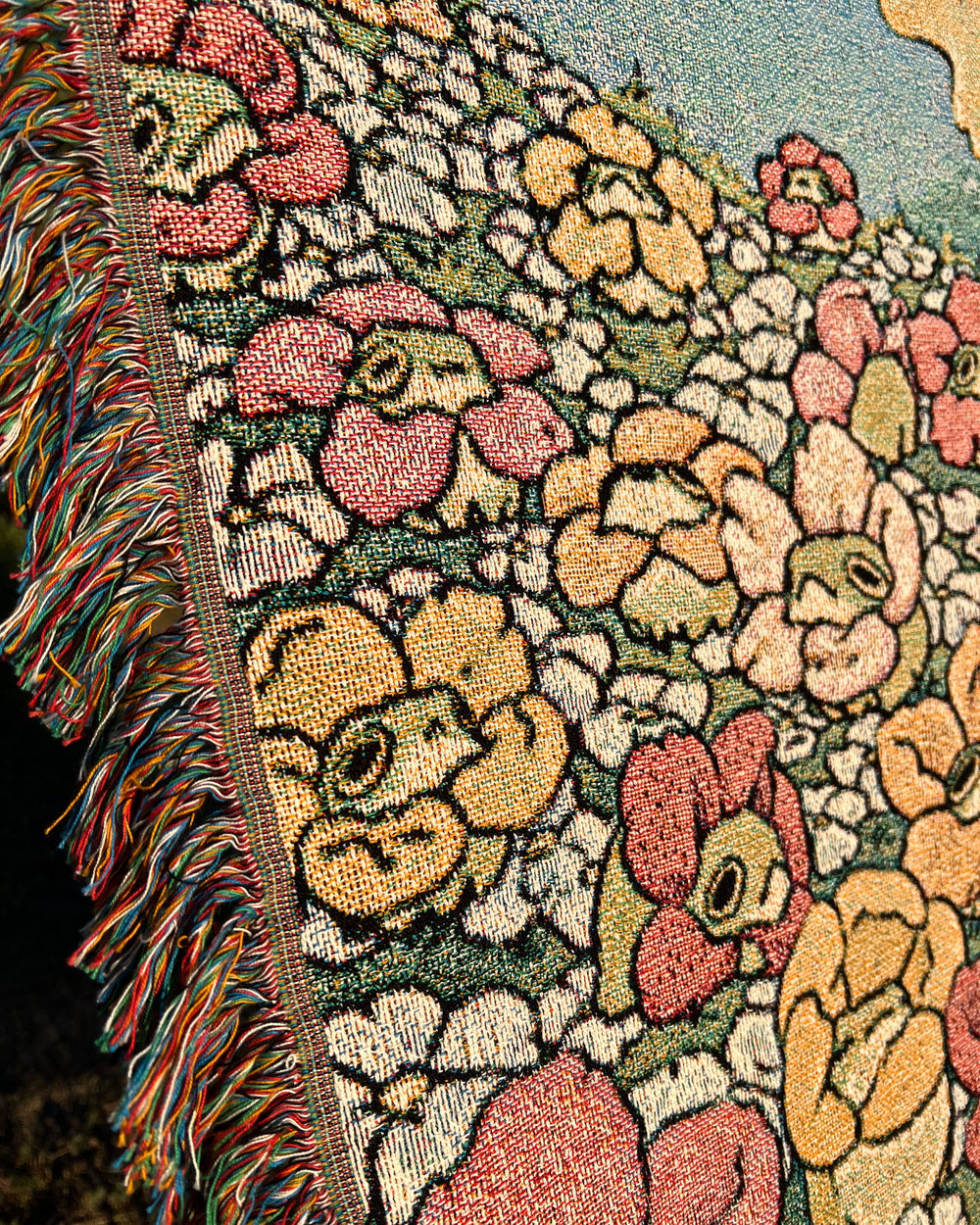 a woven blanket with a chanterelle character surrounded by frogs in flower necklaces closeup