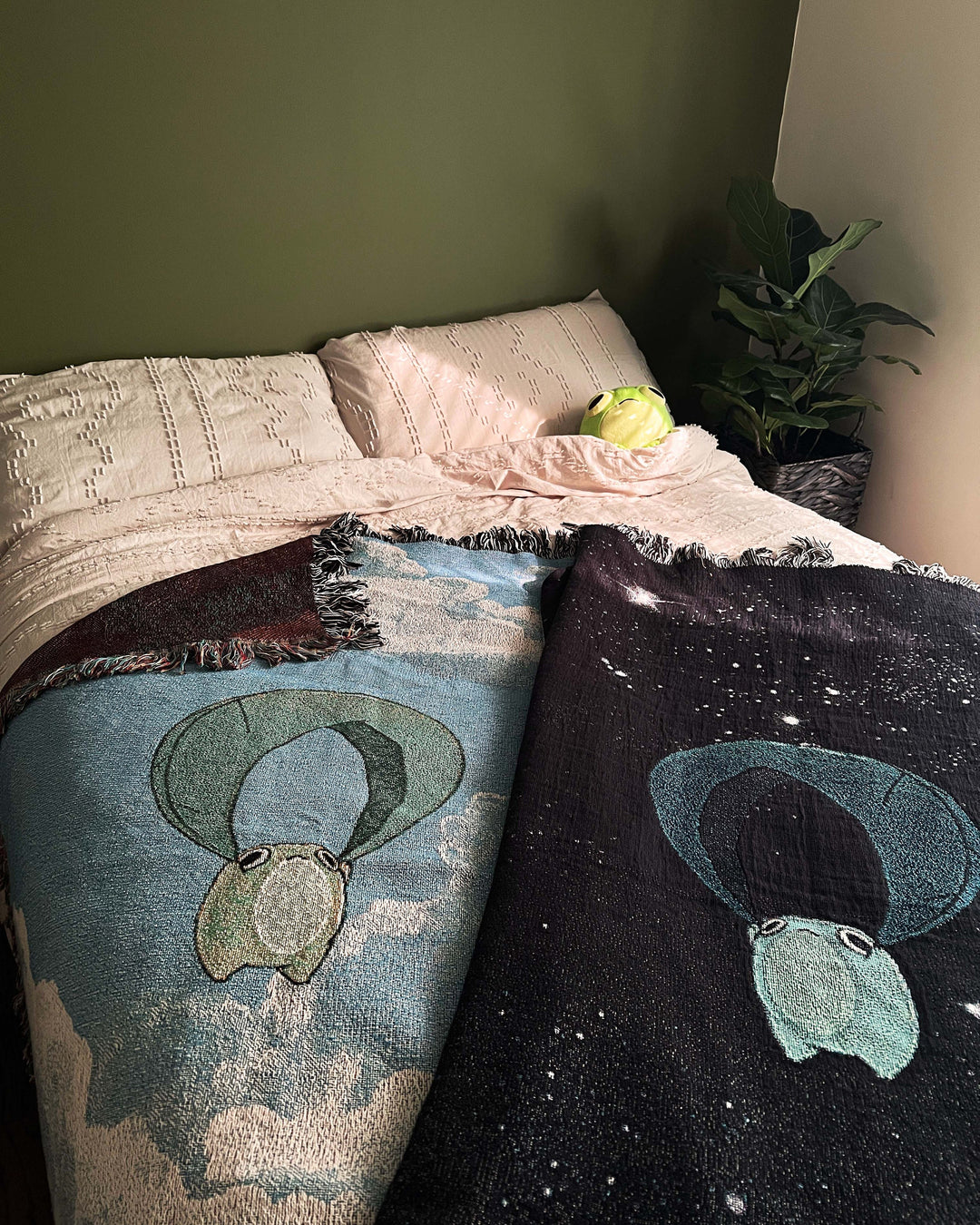 two throw blankets on a bed depicting frogs riding leaves through the sky