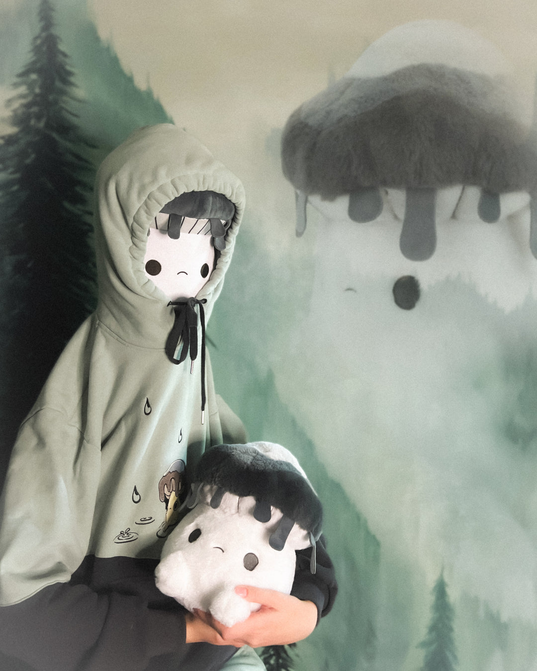 Person wearing a hooded outfit holding a plush toy with a forest background