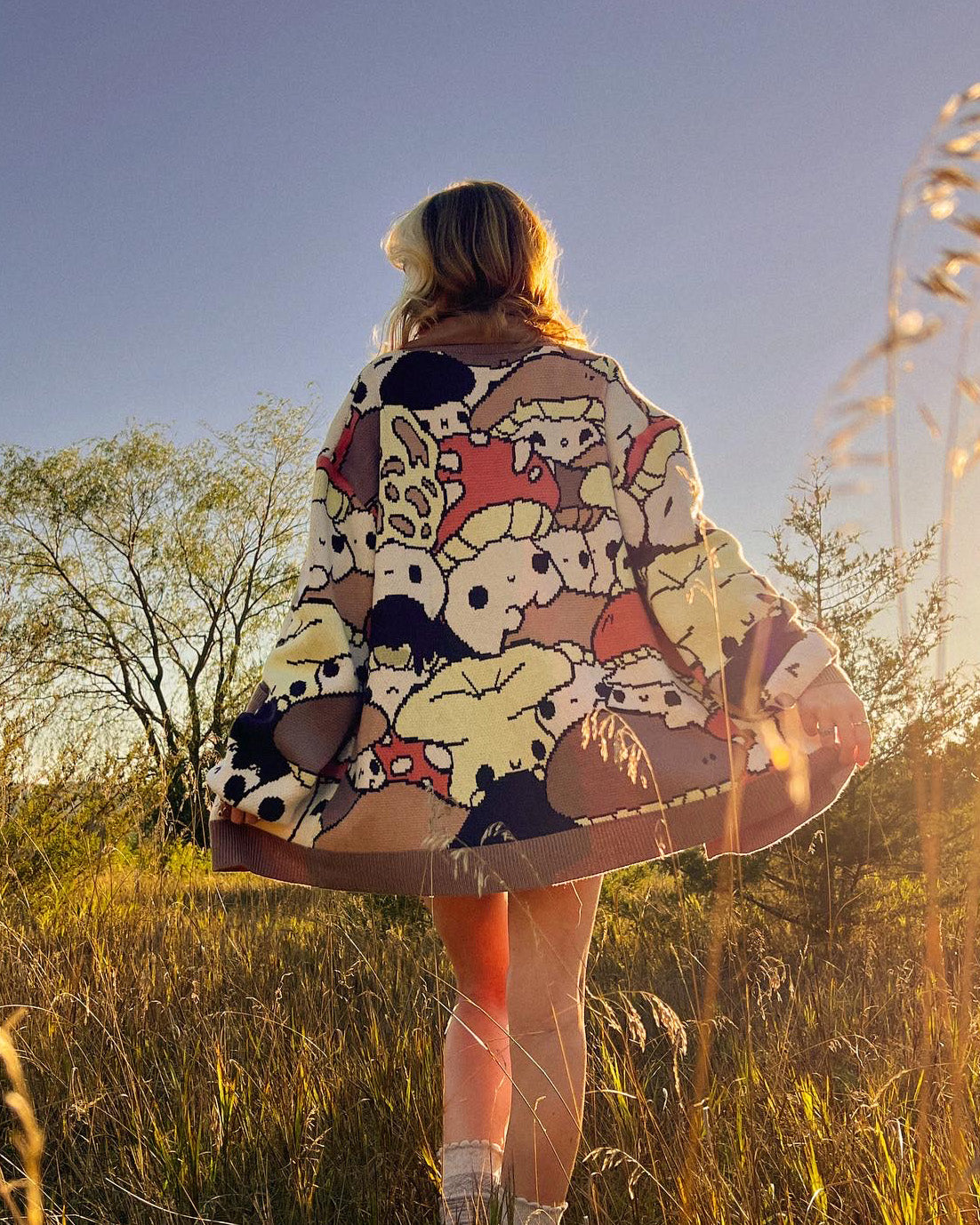 abi toads wearing a mushroom collage cardigan in a field