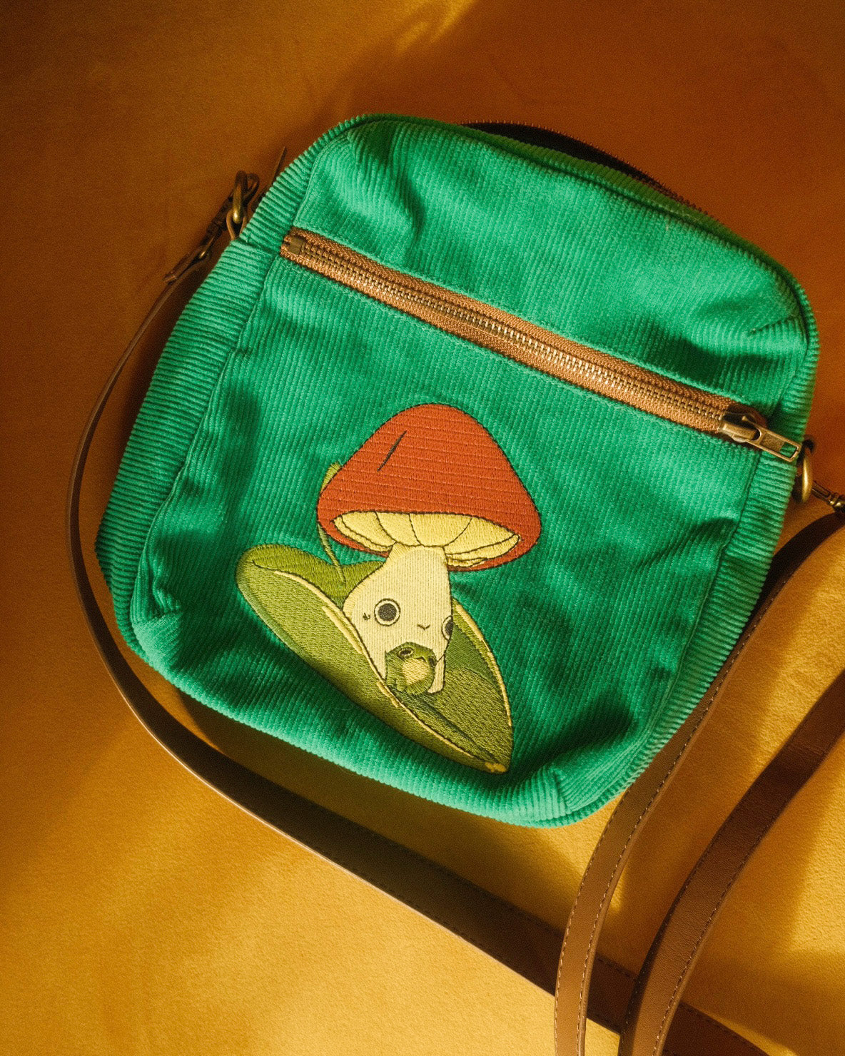 teal corduroy bag with an embroidered mushling on the front riding a leaf