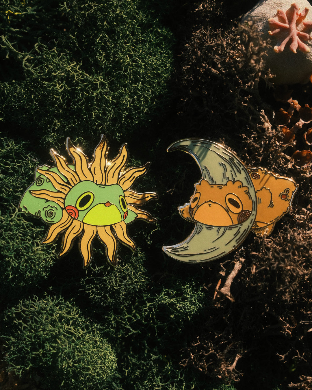 two pins of sun frog and moon toad on mossy background