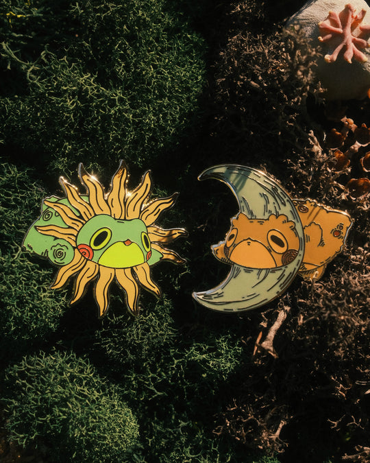 two pins of sun frog and moon toad on mossy background