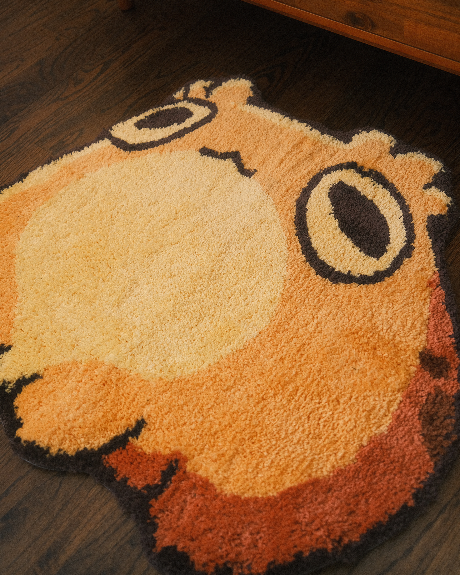 Round orange toad rug with a cartoonish design on a wooden floor